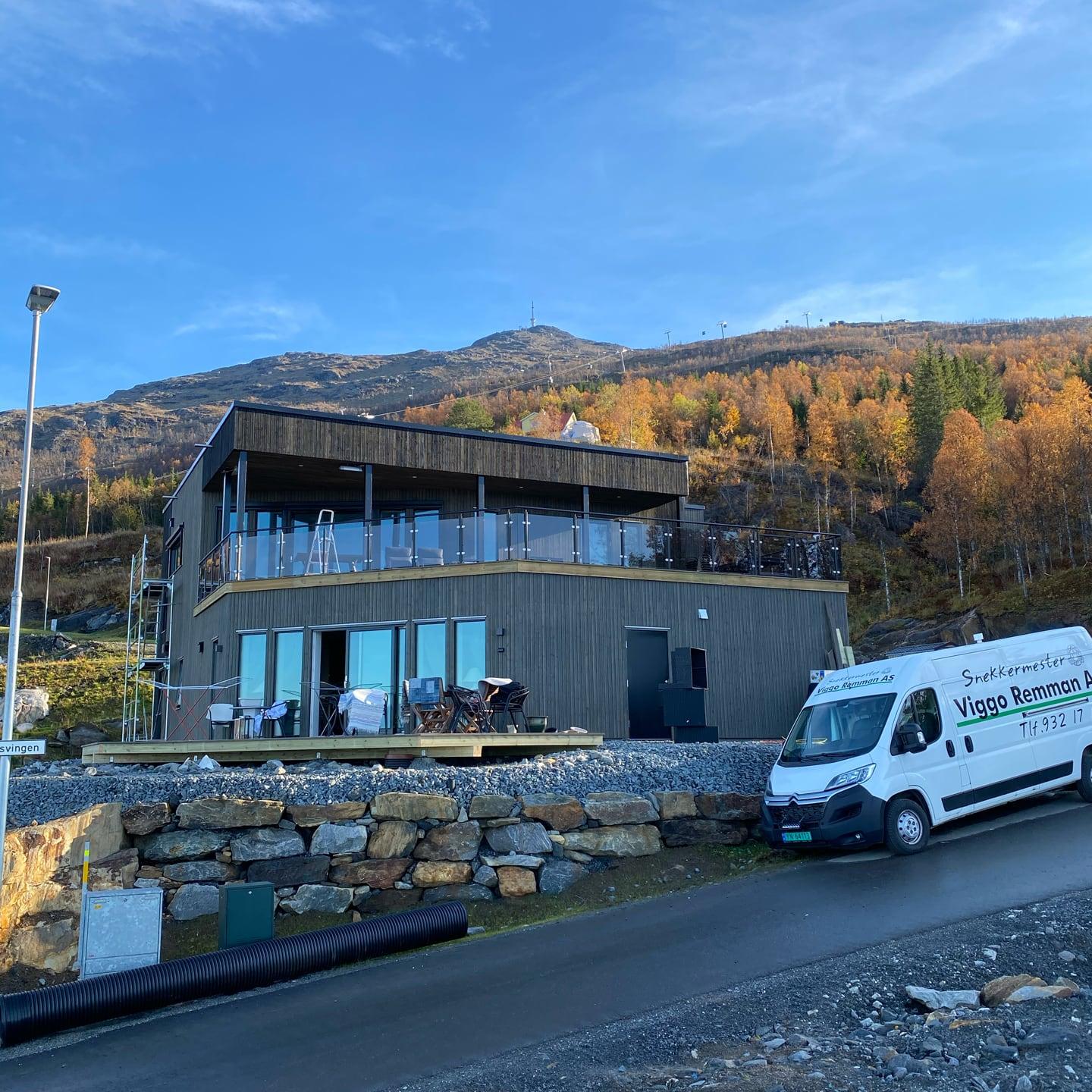 Moderne hus med store vinduer og firmabilen parkert foran, høstfjell bak