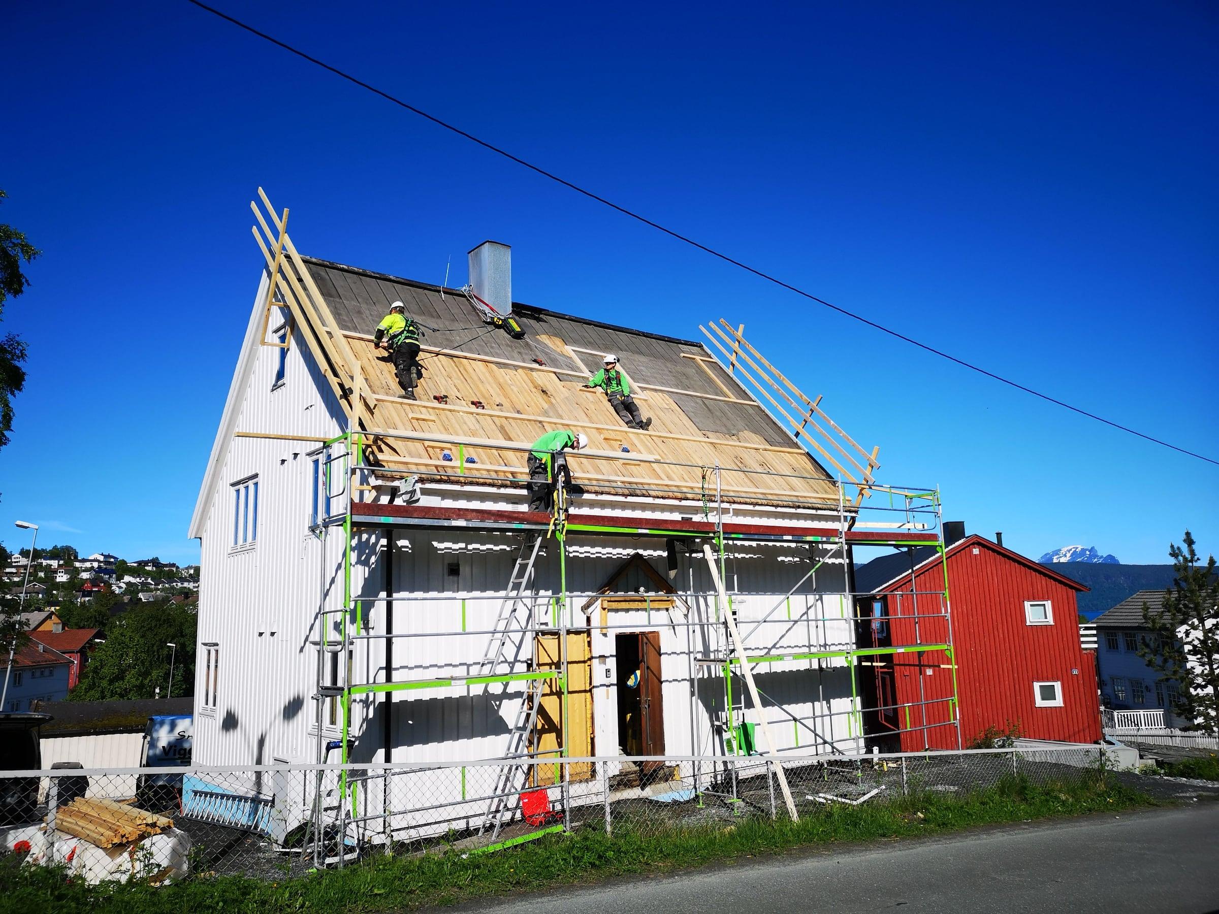 Hvitt hus med stillas og nytt undertak under arbeid